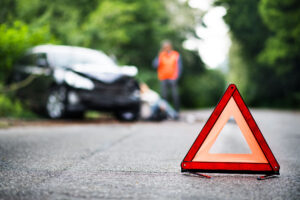 Car Accident Lawyer Derry, NH - A close up of a red emergency triangle on the road in front of a car after an accident.